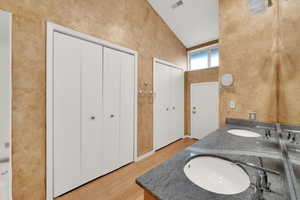 Full bathroom with light wood finished floors, high vaulted ceiling, and double vanity