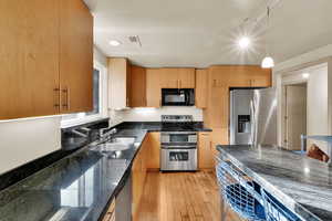 Kitchen featuring appliances with stainless steel finishes, decorative light fixtures, light wood-style flooring, and dark stone counters