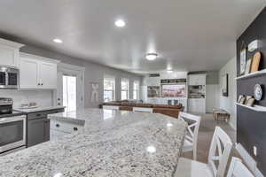 Kitchen featuring appliances with stainless steel finishes, white cabinets, light stone counters, and recessed lighting