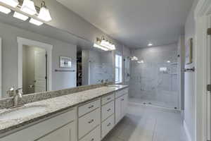 Full bath with double vanity, a marble finish shower, a spacious closet, and light tile patterned flooring