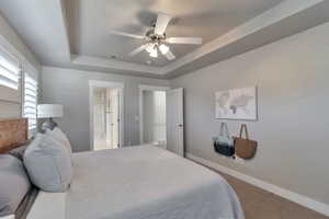 Carpeted bedroom featuring a raised ceiling, ceiling fan, and ensuite bathroom