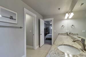 Ensuite bathroom featuring double vanity, light tile patterned flooring, and ceiling fan