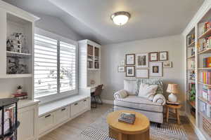 Sitting room featuring light wood-style floors, built in study area, and vaulted ceiling