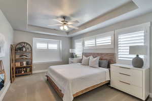 Bedroom featuring a tray ceiling, ceiling fan, and light colored carpet