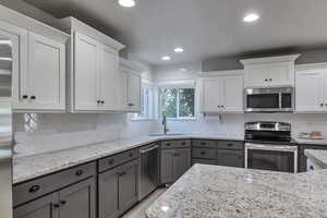 Kitchen featuring appliances with stainless steel finishes, white cabinetry, gray cabinetry, recessed lighting, and light stone countertops