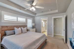 Bedroom featuring a tray ceiling, light carpet, a ceiling fan, and ensuite bathroom