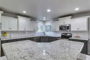 Kitchen with white cabinets, stainless steel appliances, tasteful backsplash, gray cabinets, and light stone counters