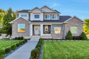 Craftsman-style home featuring a front yard, covered porch, board and batten siding, and brick siding