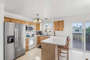 Kitchen with stainless steel appliances, a peninsula, a kitchen bar, light countertops, and hanging light fixtures