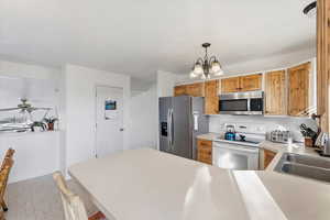 Kitchen with stainless steel appliances, light countertops, hanging light fixtures, a chandelier, and a peninsula