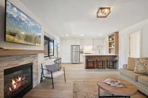 Living area with light wood-type flooring, a glass covered fireplace, and recessed lighting