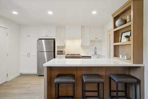 Kitchen with a kitchen bar, white cabinetry, decorative backsplash, stainless steel appliances, and a peninsula