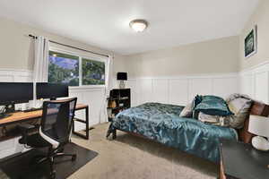 Bedroom with a decorative wall, a wainscoted wall, an office area, and light carpet