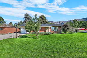 Ranch-style home featuring a front yard, concrete driveway, a mountain view, an attached garage, and brick siding