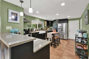 Kitchen with dark cabinets, light stone counters, a peninsula, hanging light fixtures, and stainless steel fridge with ice dispenser
