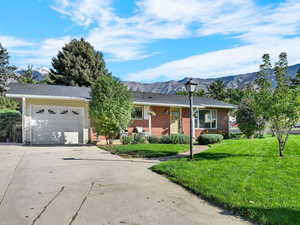 Single story home featuring a front lawn, driveway, a mountain view, an attached garage, and brick siding