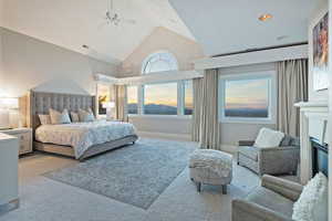 Bedroom with carpet flooring, high vaulted ceiling, ceiling fan, and a glass covered fireplace
