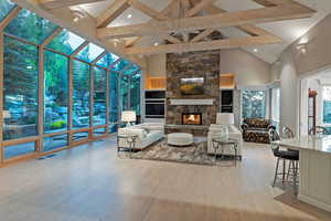 Living room with a stone fireplace, light wood-type flooring, high vaulted ceiling, beamed ceiling, and a sunroom