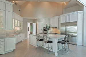 Kitchen featuring decorative backsplash, appliances with stainless steel finishes, a breakfast bar area, white cabinets, and light stone counters