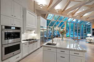 Kitchen with appliances with stainless steel finishes, white cabinetry, open floor plan, beam ceiling, and light stone counters