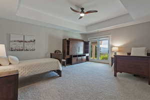 Bedroom with a raised ceiling, access to outside, carpet flooring, and a ceiling fan