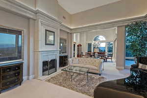 Carpeted living area with a fireplace with raised hearth, a chandelier, and a high ceiling
