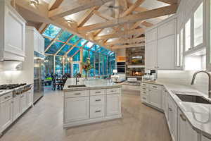 Kitchen featuring backsplash, an island with sink, white cabinets, beamed ceiling, and high vaulted ceiling