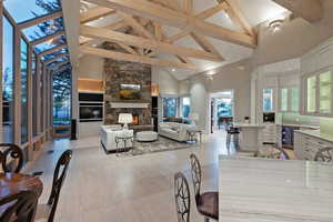 Living room with high vaulted ceiling, a stone fireplace, beamed ceiling, light wood finished floors, and beverage cooler