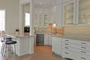 Bar with white cabinets, beverage cooler, glass insert cabinets, decorative backsplash, and light stone countertops