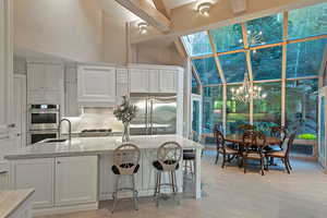Kitchen featuring white cabinetry, a skylight, appliances with stainless steel finishes, a high ceiling, and light stone counters