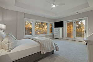 Carpeted bedroom with a tray ceiling, access to exterior, and a ceiling fan