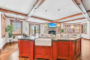 Kitchen with dark brown cabinets, an island with sink, finished concrete floors, hanging light fixtures, and beamed ceiling