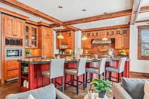 Kitchen featuring open shelves, decorative light fixtures, glass insert cabinets, beam ceiling, and a kitchen breakfast bar