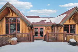 Snow covered rear of property with french doors, a deck, board and batten siding, and a metal roof