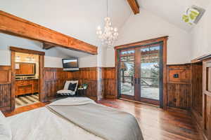 Bedroom with beamed ceiling, wood-type flooring, wainscoting, a chandelier, and access to exterior