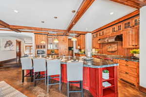 Kitchen with beamed ceiling, glass insert cabinets, ventilation hood, a breakfast bar, and decorative light fixtures