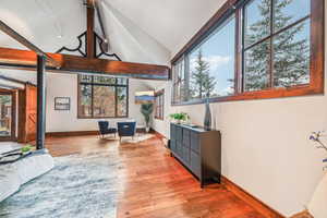Living room featuring healthy amount of natural light, light wood-style flooring, high vaulted ceiling, a barn door, and beamed ceiling