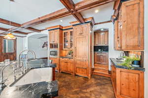 Kitchen featuring coffered ceiling, beam ceiling, concrete floors, arched walkways, and brown cabinetry