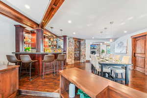 Dining space with dark wood-style floors, a dry bar, beamed ceiling, recessed lighting, and a stone fireplace