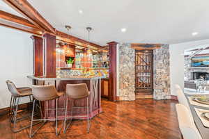 Indoor wet bar with dark wood-style flooring, pendant lighting, a stone fireplace, recessed lighting, and dark brown cabinets