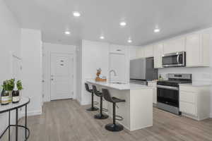 Kitchen featuring a peninsula, a breakfast bar, stainless steel appliances, light wood finished floors, and white cabinets
