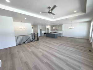 Unfurnished living room with a chandelier, light wood-style floors, recessed lighting, a raised ceiling, and a ceiling fan