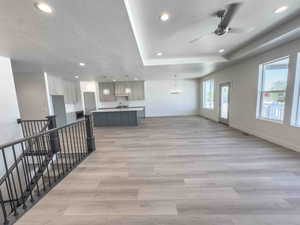 Unfurnished living room featuring recessed lighting, a textured ceiling, a chandelier, a tray ceiling, and light wood-style floors