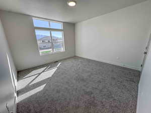 Carpeted spare room with a textured ceiling and baseboards