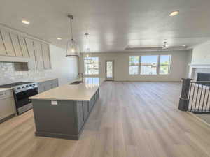 Kitchen with stainless steel gas stove, decorative light fixtures, tasteful backsplash, gray cabinets, and open floor plan