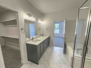 Full bath featuring double vanity, a garden tub, a stall shower, and light marble finish floors