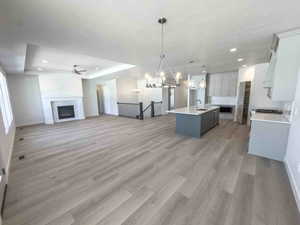 Kitchen featuring open floor plan, a fireplace, hanging light fixtures, a chandelier, and a kitchen island with sink