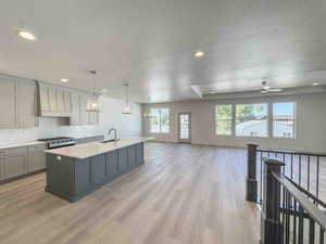 Kitchen with gray cabinetry, hanging light fixtures, a center island with sink, stainless steel gas stove, and a textured ceiling