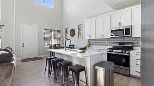 Kitchen with stainless steel appliances, healthy amount of natural light, white cabinets, a center island with sink, and a high ceiling