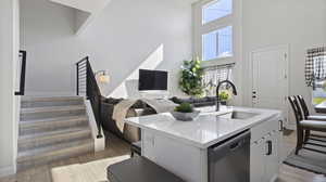 Kitchen with dishwasher, light wood finished floors, a towering ceiling, an island with sink, and white cabinetry